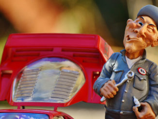 Spielzeugfigur eines mürrisch dreinblickenden Automechanikers neben einem Spielzeugauto.