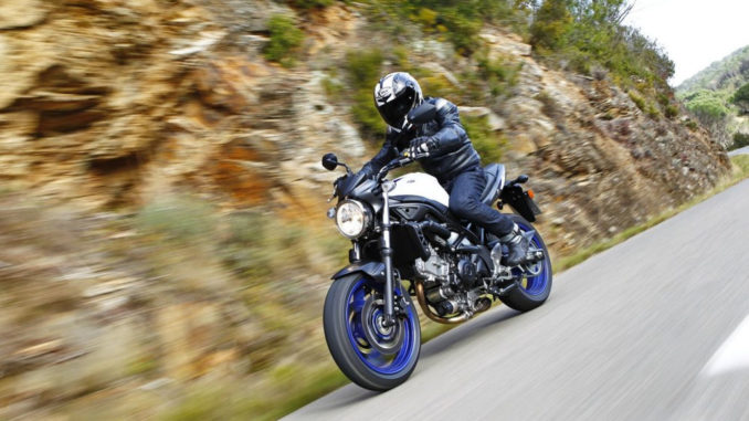 Eine schwarze Suzuki SV650 mit blauen Rädern fährt auf einer Landstraße.