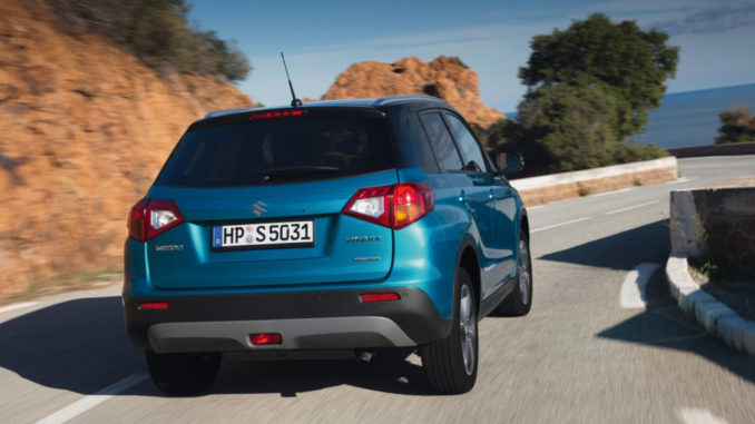 Blick auf das Heck eines blauen Suzuki Vitara bei der Anfahrt auf eine Kurve einer Landstraße