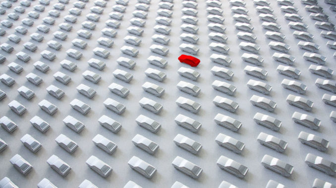 Eine Reihe weißer Autos aus Pappe, nur eines ist rot