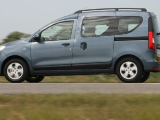 Ein blau-grauer Dacia Dokker fährt auf einer Landstraße vor einem sommerlichen Rapsfeld.