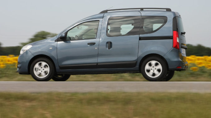 Ein blau-grauer Dacia Dokker fährt auf einer Landstraße vor einem sommerlichen Rapsfeld.