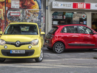 Ein gelber und ein roter Renault Twingo der dritten Generation stehen auf der Straße einer Großstadt.