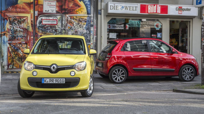 Ein gelber und ein roter Renault Twingo der dritten Generation stehen auf der Straße einer Großstadt.