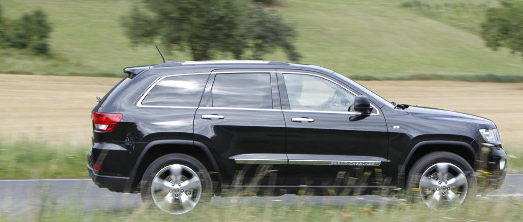 Ein schwarzer Jeep Grand Cherokee Overland Summit fährt auf der Landstraße.