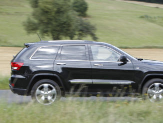 Ein schwarzer Jeep Grand Cherokee Overland Summit fährt auf der Landstraße.