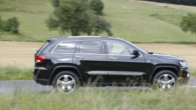 Ein schwarzer Jeep Grand Cherokee Overland Summit fährt auf der Landstraße.