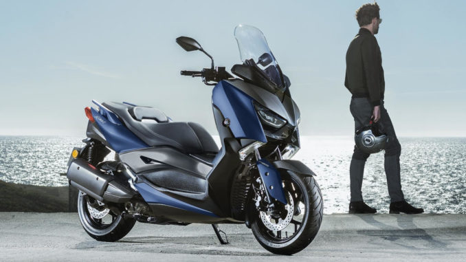 Eine blaue Yamaha X-Max 300 steht 2018 auf einer Asphaltfläche vor Meereskulisse.