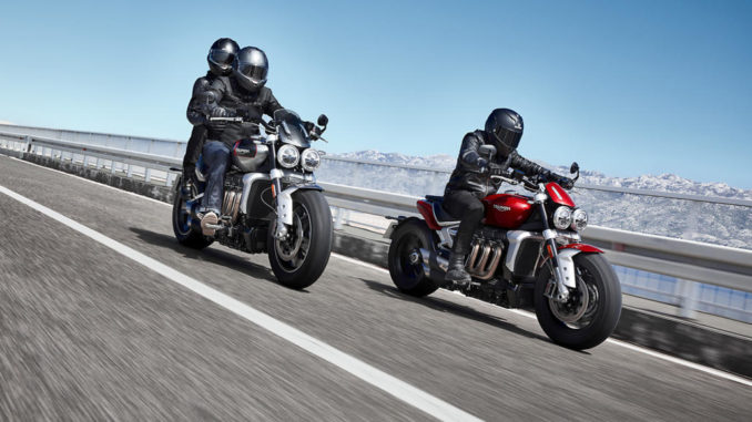 Eine graue Triumph Rocket 3 GT und eine rote Rocket 3 R fahren 2019 auf einer Küstenstraße.