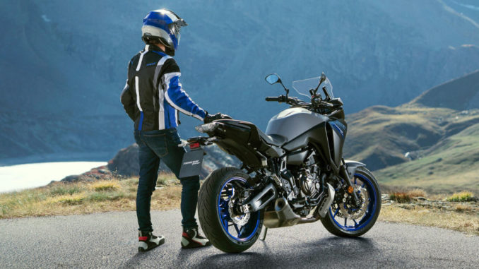 Ein Motorradfahrer steht 2020 mit einer blau-grauen Yamaha Tracer 700 an der Kurve eine Bergpasses.