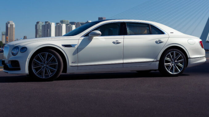 Ein weißer Bentley Flying Spur steht 2022 vor der Skyline von Rotterdam.