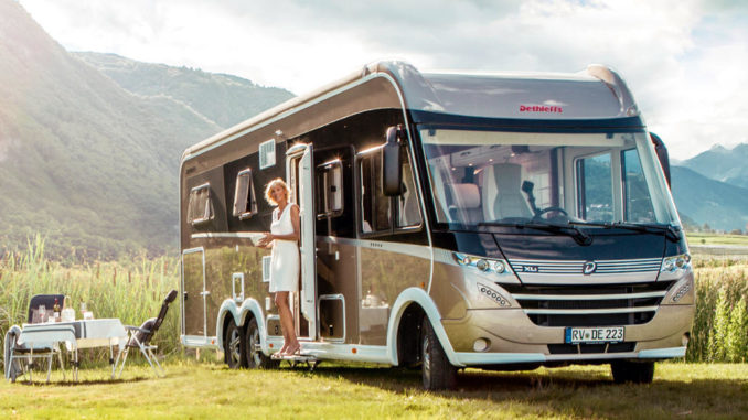 Ein beiges Dethleffs-Wohnmobil vom Typ Globetrotter XLI (MJ 2019) steht neben einem Campingtisch in einem Naturpark.