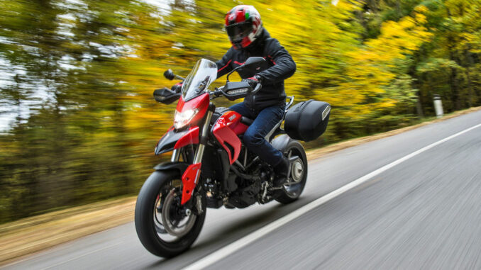 Eine rote Ducati Multistrada fährt 2016 auf einer Straße durch den Herbstwald.