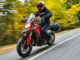 Eine rote Ducati Multistrada fährt 2016 auf einer Straße durch den Herbstwald.