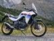 Eine weiße Honda XL 750 Transalp steht 2023 auf einer Schotterpiste in den Alpen.
