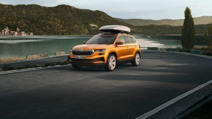 Ein orangener Skoda Karoq mit der Dachgepäckbox "Skoda Roof Box 400L" fährt auf einer Passstraße.