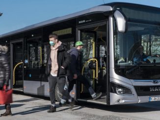 Ein silberner Omnibus vom Typ MAN Lion's City steht an einer Haltestelle in München.