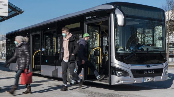 Ein silberner Omnibus vom Typ MAN Lion's City steht an einer Haltestelle in München.