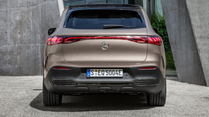 Mercedes_EQE_SUV_2022 Ein Mercedes-EQ. EQE SUV. AMG Line Exterior, Night Package, Velvet brown metallic, steht 2022 vor einem Gebäude aus Beton.
