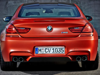 Das neue BMW M6 Coupé in Orange steht vor einer Betonwand (12/2014).