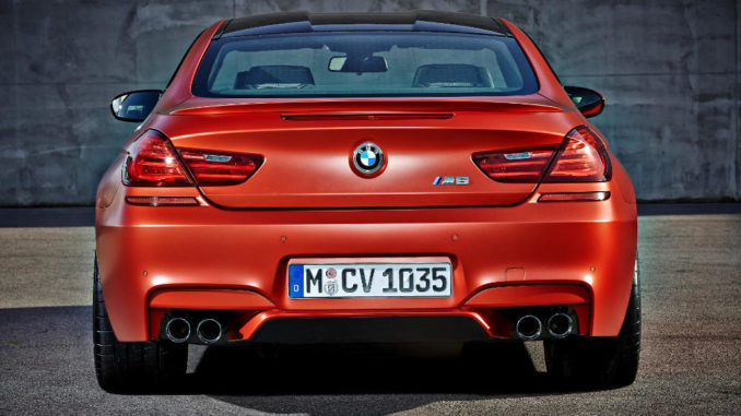 Das neue BMW M6 Coupé in Orange steht vor einer Betonwand (12/2014).