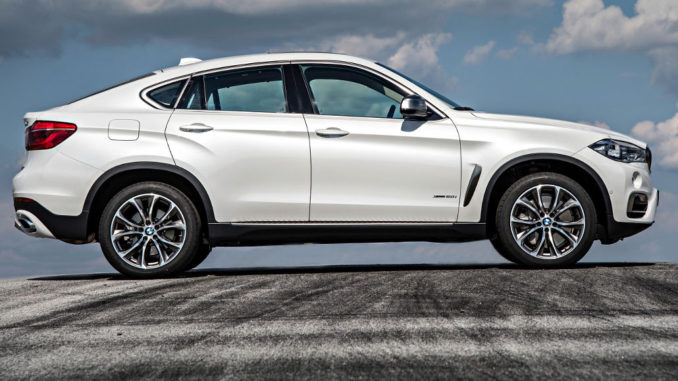 Ein weißer BMW X6 xDrive50i (F16 von 10/2014) aufgenommen im Profil steht auf einer Asphaltfläche mit Reifenspuren.