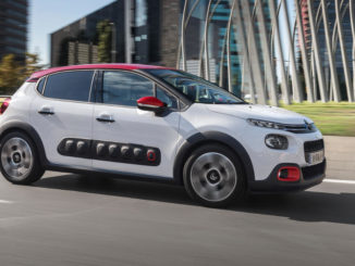 Ein weißer Citroen C3 (3. Generation) fährt an Bürogebäuden vorbei.