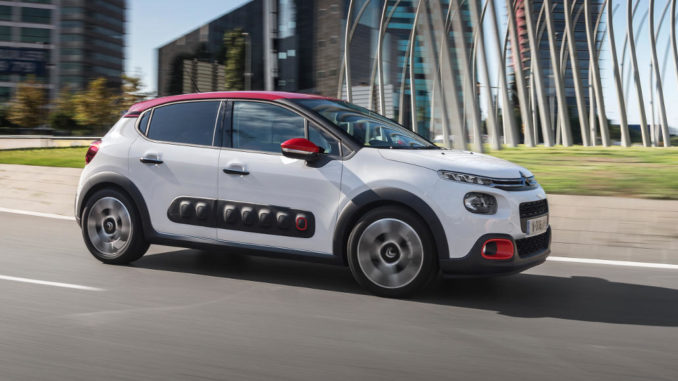 Ein weißer Citroen C3 (3. Generation) fährt an Bürogebäuden vorbei.