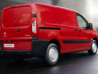 Ein roter Citroen Jumpy fährt in einer Stadt über eine nasse Straße.