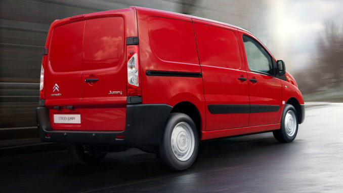 Ein roter Citroen Jumpy fährt in einer Stadt über eine nasse Straße.