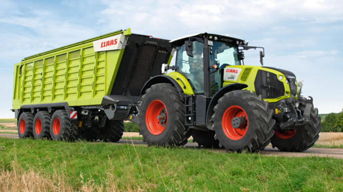 Straßentransport eines grünen Claas Axion 800 mit einem Häckseltransportwagen vom Typ Cargos 700.