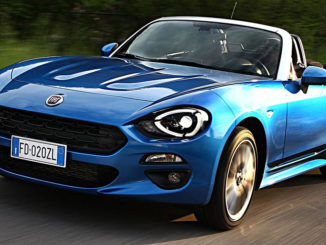 Ein blauer Fiat 124 Spider fährt auf einer italienischen Landstraße.