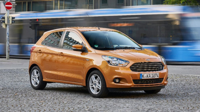 Ein bronze-farbener Ford Ka+ steht 2016 auf einem Platz in München, an dem eine Trambahn vorbeifährt.