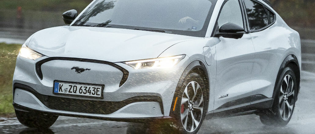 Ein weißer Ford Mustang Mach-E fährt 2021 auf regennasser Fahrbahn.