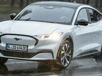 Ein weißer Ford Mustang Mach-E fährt 2021 auf regennasser Fahrbahn.