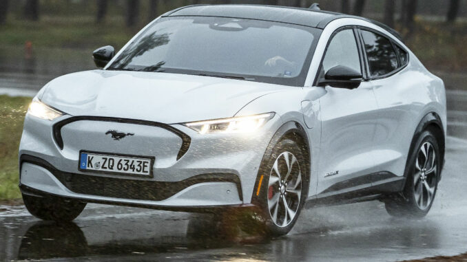 Ein weißer Ford Mustang Mach-E fährt 2021 auf regennasser Fahrbahn.