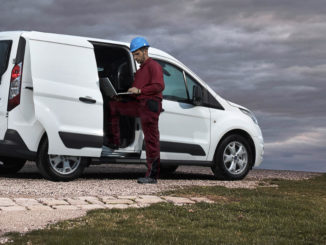 Ein Bauarbeiter mit Laptop steht 2013 vor einem weißen Ford Transit Connect mit geöffneter Seitentür