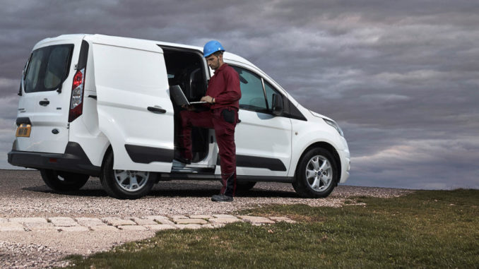 Ein Bauarbeiter mit Laptop steht 2013 vor einem weißen Ford Transit Connect mit geöffneter Seitentür