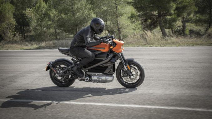 Eine orangene Harley-Davidson Livewire fährt 2020 auf einer Landstraße am Waldrand.