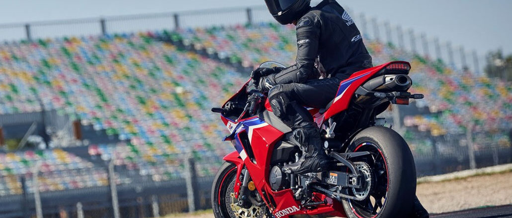 Ein Motorradfahrer sitzt 2024 wartend auf einer roten Honda CBR600RR vor einer Rennstreckentribüne.
