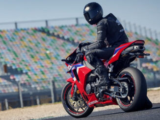 Ein Motorradfahrer sitzt 2024 wartend auf einer roten Honda CBR600RR vor einer Rennstreckentribüne.