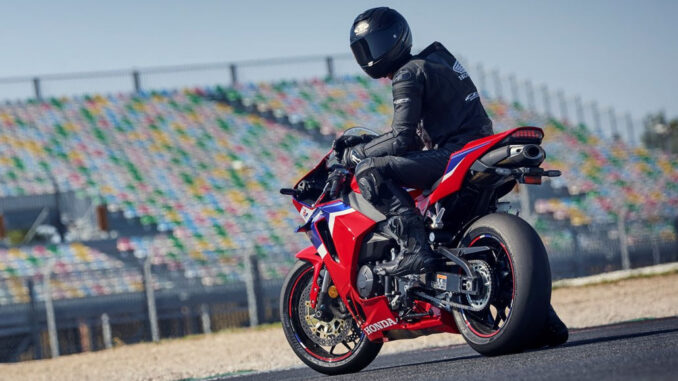 Ein Motorradfahrer sitzt 2024 wartend auf einer roten Honda CBR600RR vor einer Rennstreckentribüne.