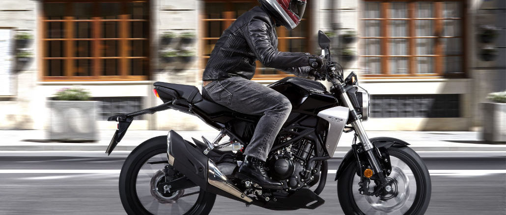 Eine schwarze Honda CB300R fährt 2017 an einem älteren Bürogebäude vorbei.