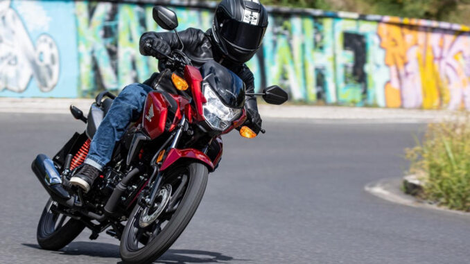 21YM HONDA CB125F in rot fährt an einer Mauer mit Graffitis vorbei.