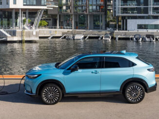 Ein blauer Honda e:Ny1 steht 2023 an einer Ladesäule an einem Hafen.