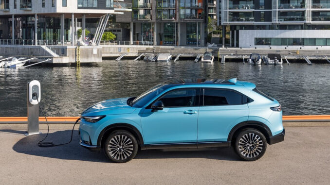 Ein blauer Honda e:Ny1 steht 2023 an einer Ladesäule an einem Hafen.