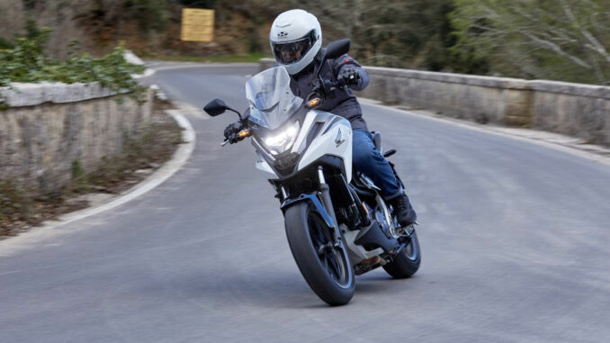 21YM HONDA NC750X in weiß-blau auf einer Bergstraße. One of Europe’s favourite all-rounders gets a well-rounded evolution: more power for the engine, plus higher redline and revised gearbox ratios, which come hand-in-hand with Throttle By Wire management, 3 riding modes and refined, expanded Honda Selectable Torque Control. Its renowned fuel efficiency is maintained, and a full 6kg has been shaved from the kerb weight. A redesigned frame is clothed in sharper-edged styling, the unique up-front storage compartment is usefully larger and seat height 30mm lower. The Dual Clutch Transmission variant continues to offer a technology unique to Honda on two wheels. A new screen, LED lighting and LCD dash round out the update.