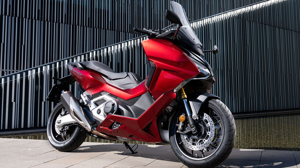 Eine rote Honda NSS 750 Forza steht 2021 vor einem Brunnen.