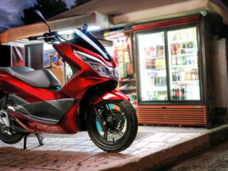 Eine rote Honda PCX125 steht abends vor einem Kiosk.