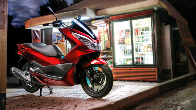 Eine rote Honda PCX125 steht abends vor einem Kiosk.